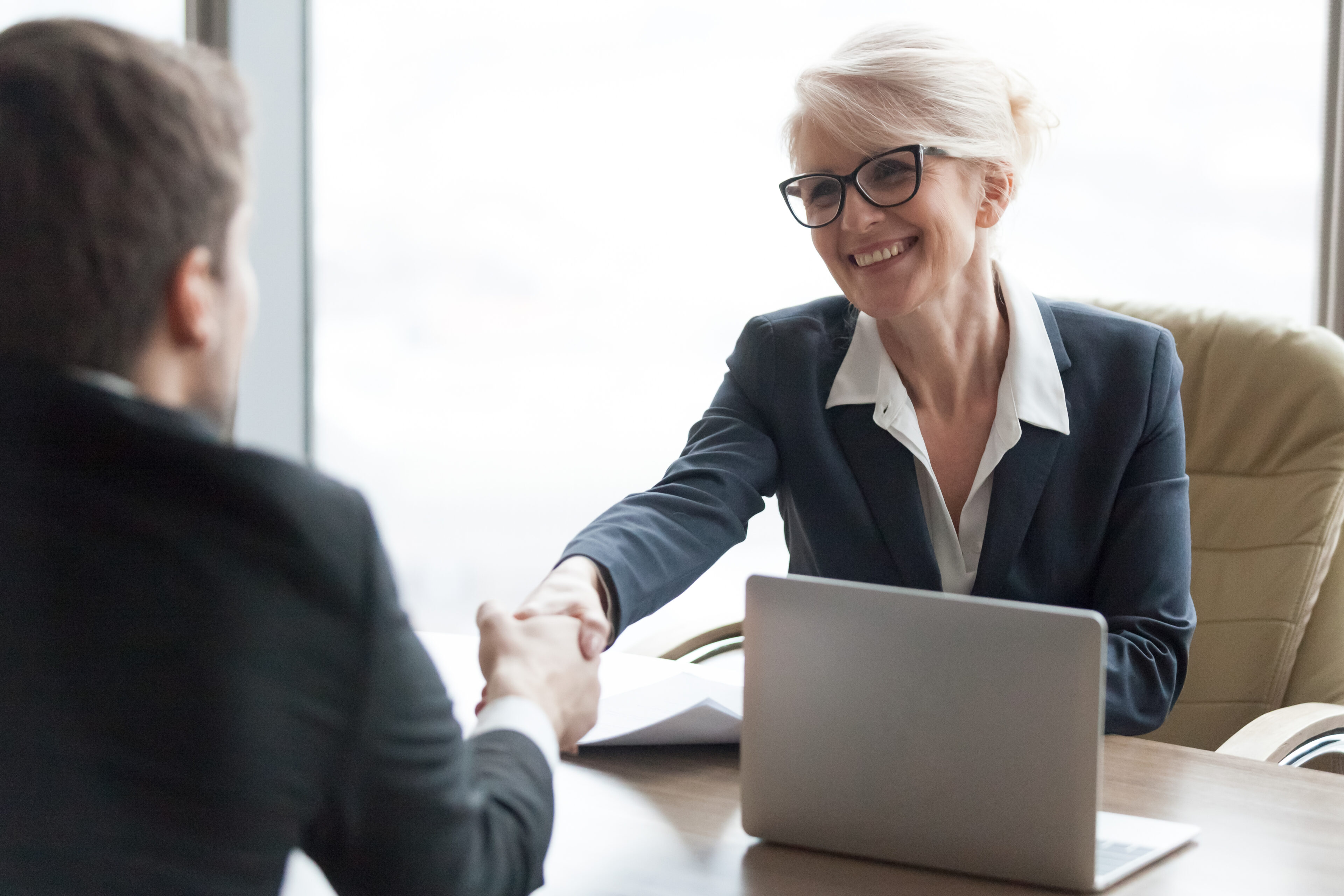 Friendly smiling hr manager handshaking applicant hiring candidate at job interview, happy executive businesswoman shaking businessman hand welcoming at meeting negotiation making business deal