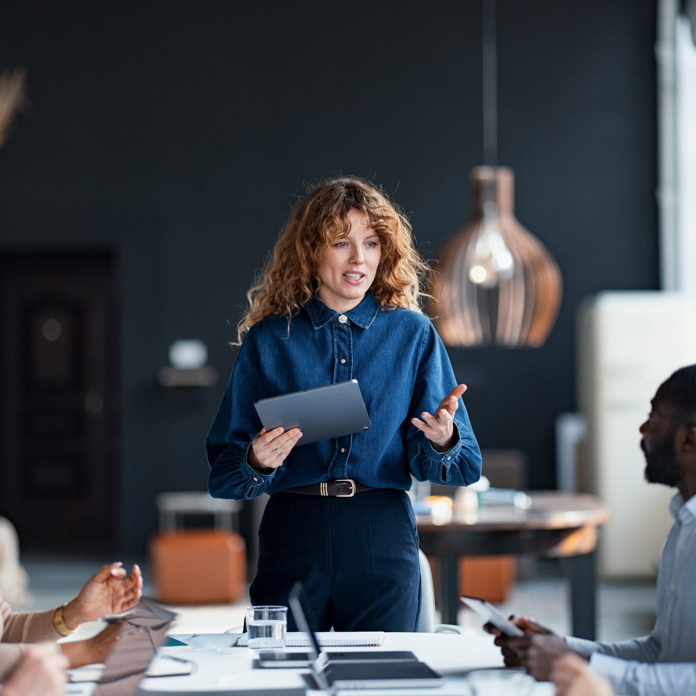 Confident businesswoman presents to a diverse team during a collaborative meeting in a stylish office environment, promoting teamwork and communication.